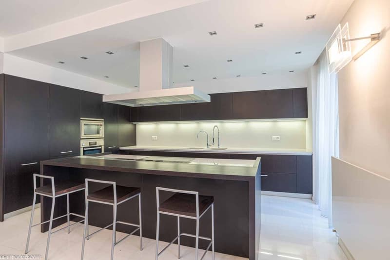 Island with stools, modern cabinets, appliances, marble countertops, and recessed lighting.