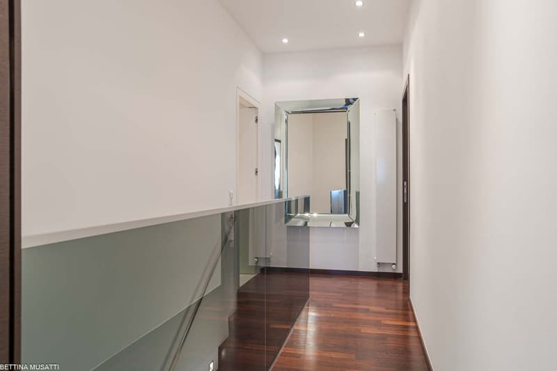 Empty corridor with glass railings, mirror, radiators, and wooden floors