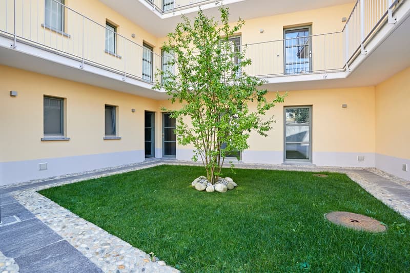 Balconies with railings, a small garden, well-maintained grass and shrubs, and walkways