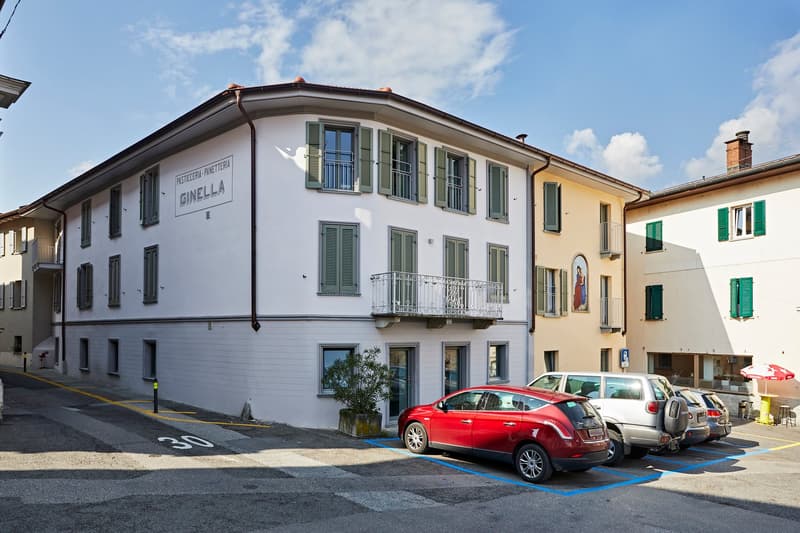 2 story white building, multiple windows, balcony on second floor, cars parked in front