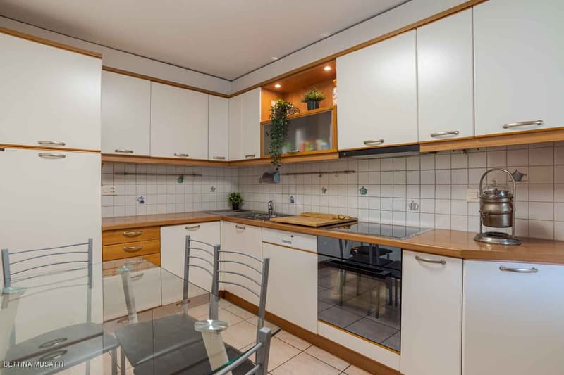 Modern white kitchen with wooden countertops, built-in appliances, tiled flooring, and a dining table with chairs.