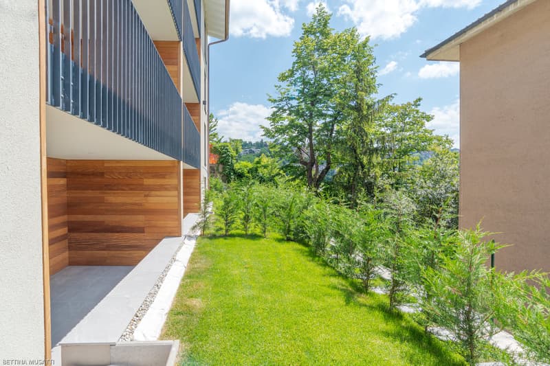 Building exterior with metal railing, wooden wall, small garden