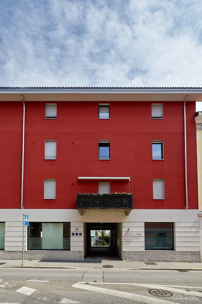 Multistory building, red exterior walls, balcony, double doors as entrance, windows with shutters, side glass panels