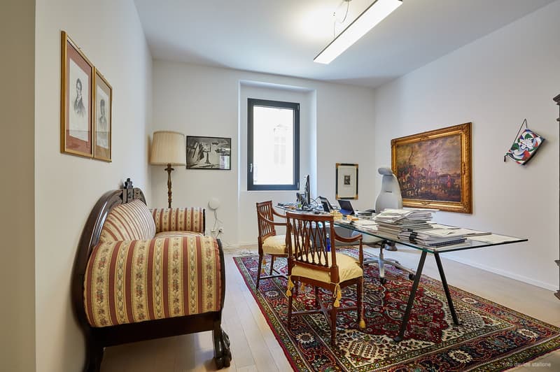 modern office with white walls, hardwood floors, wooden sofa, wooden chairs, desk with office supplies, framed paintings, and a rug