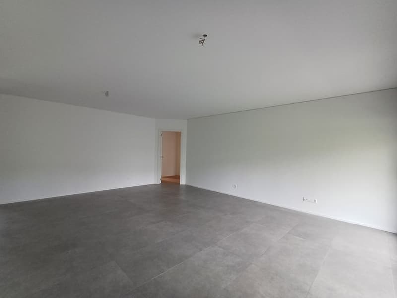 Large, open room with gray tile flooring, white walls, and a doorway leading to another room.