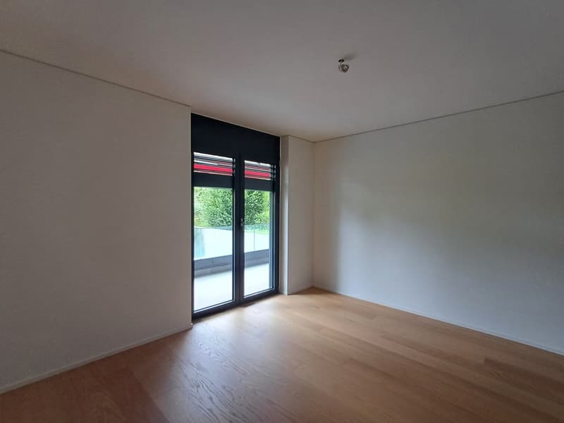 Light wooden floors, white walls, black sliding doors leading to balcony, surveillance camera on ceiling