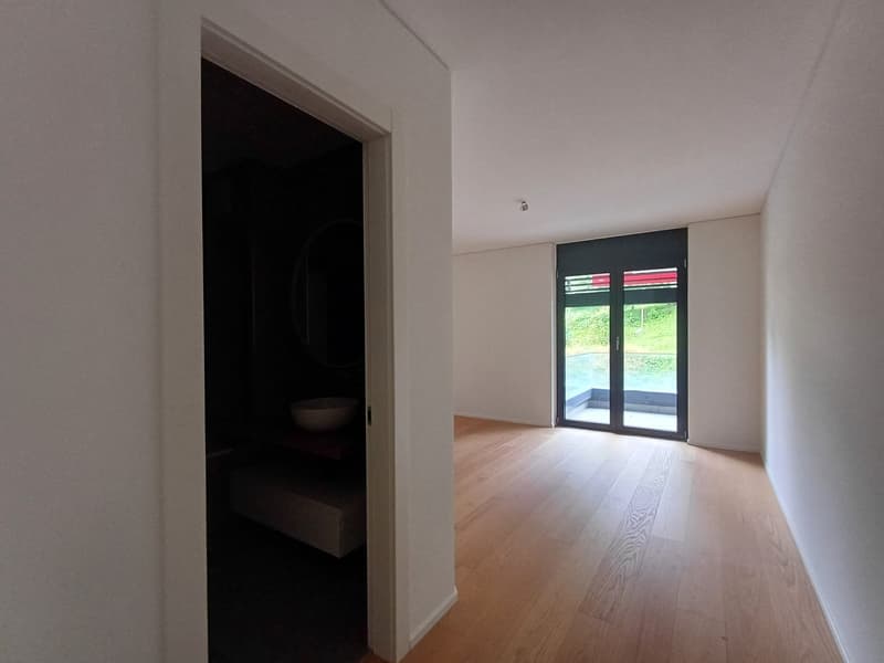 Spacious room with hardwood flooring, white walls, and a large window leading to a balcony or terrace. The room appears to be empty, providing a clean and minimalist look.