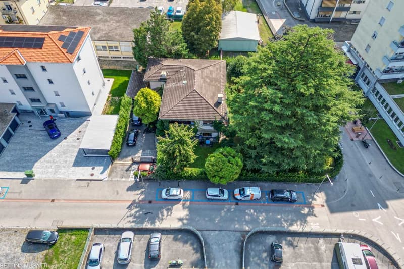 3 buildings, multiple cars parked in front, 1 covered parking, house with garage, trees, and solar panels on the rooftop