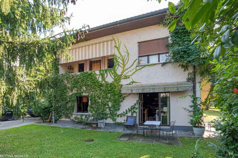 Two story house, beige exterior, green plant covering, large yard, outdoor seating, balcony, car parking