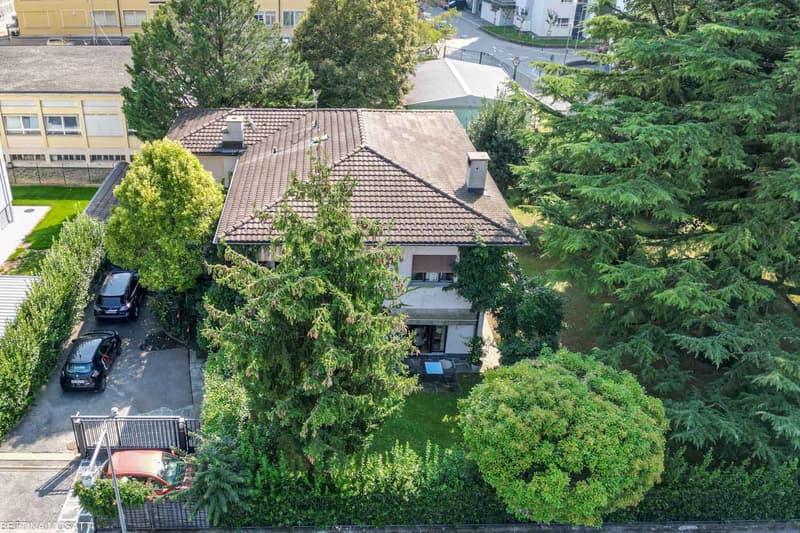 2-story house, brown roof, large garden, 2 cars parked in front, entrance from the left