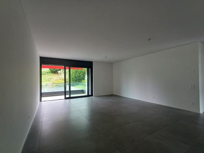 Large open living space with sliding glass doors leading to a balcony or terrace, white walls, and concrete flooring