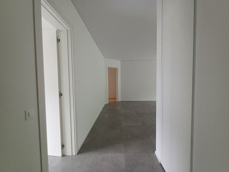 White walls, gray flooring, two doors, one leading to an empty room