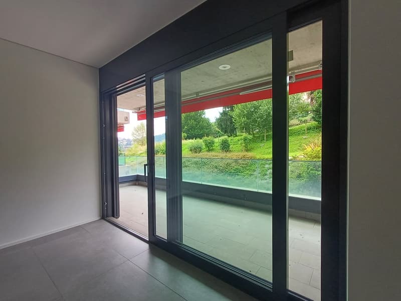 Large sliding glass doors with a view of a green outdoor area, hardwood floors, minimalist decor