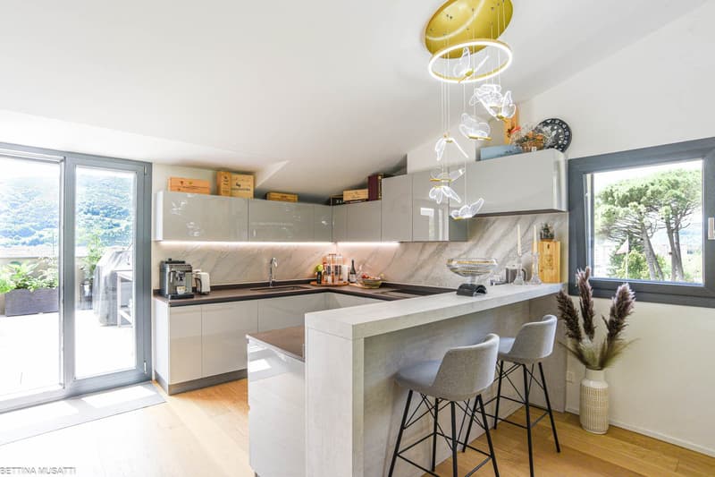 modern kitchen with large windows, marble countertop, breakfast bar, grey chairs, island with built-in appliances, plants, glass doors, balcony, chandelier