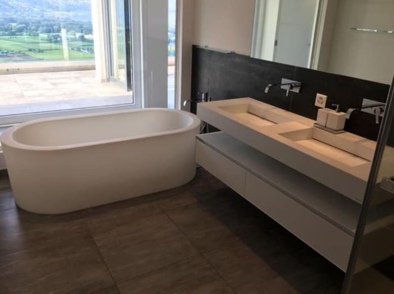 Modern bathroom with large bathtub, underfloor heating, double sinks, large mirror, tiled flooring