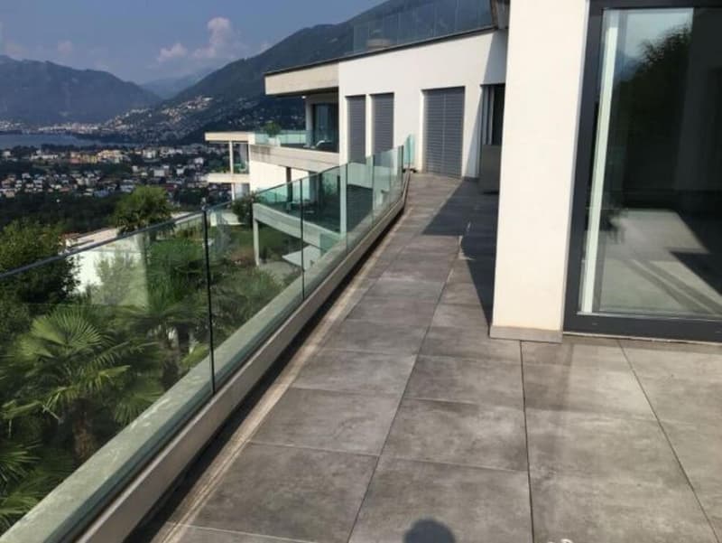 Balcony with glass railings, tiled flooring, view of mountains and buildings