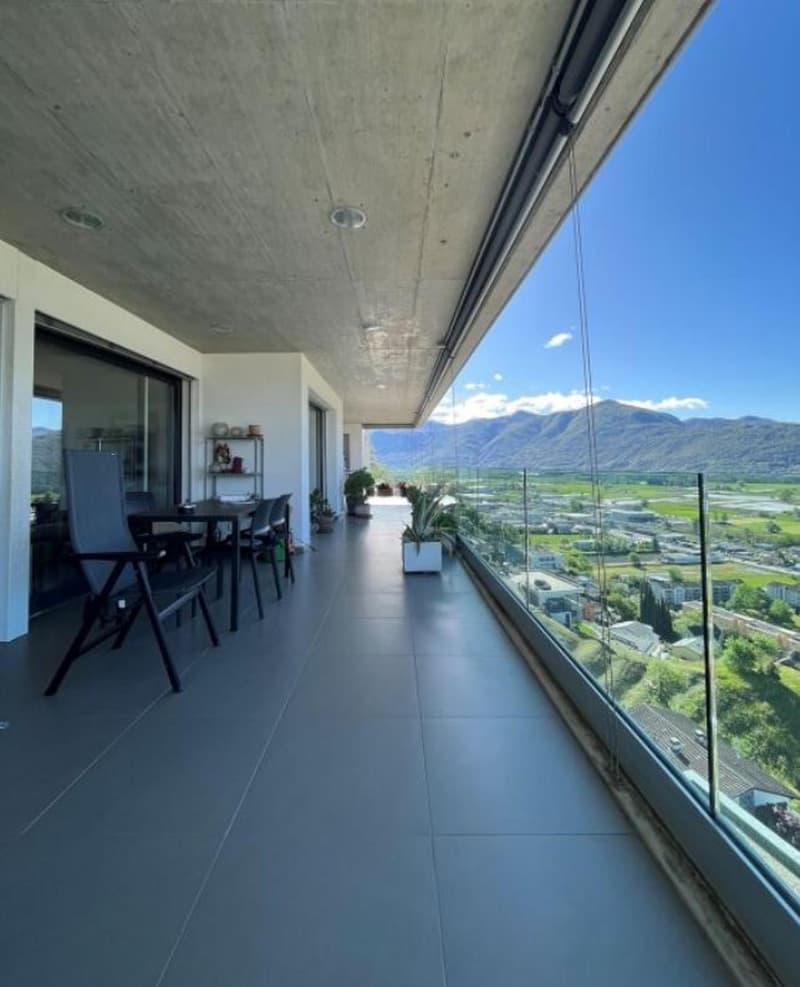 Balcony with large glass walls and balcony table, offering panoramic view of mountains