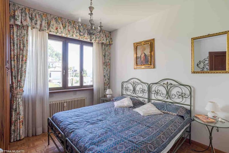 Spacious bedroom with a large bed, ornate metal headboard, floral curtains, and a balcony with a view
