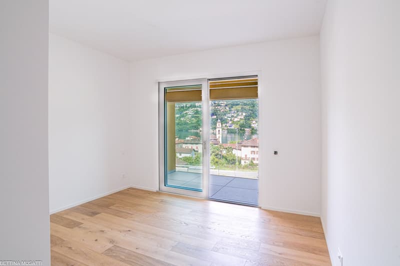 Spacious room with large windows offering a scenic view of the town and lake. The room has hardwood flooring and white walls, providing a bright and airy atmosphere.