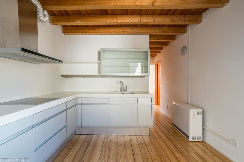 Spacious kitchen with white cabinets, wooden beams on the ceiling, hardwood flooring, and a dishwasher visible.