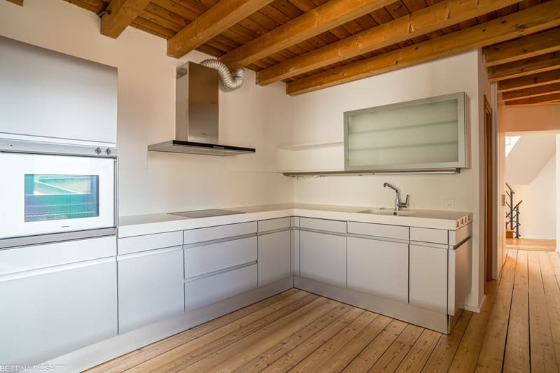 Spacious kitchen with wooden beamed ceiling, white cabinets, stainless steel appliances including a range hood and dishwasher, and hardwood flooring.