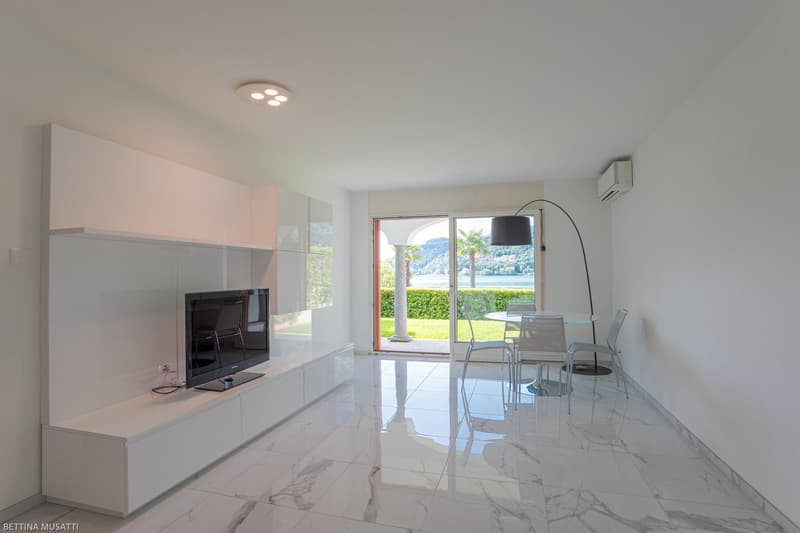 Spacious living room with large windows overlooking a scenic outdoor view, modern white furniture including a TV stand and dining table, and sleek tile flooring.