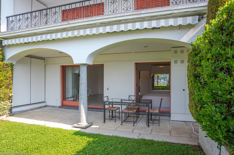 Ground floor apartment with a balcony or terrace, white exterior walls, arched entryways, wrought iron railings, and outdoor seating area with a table and chairs.