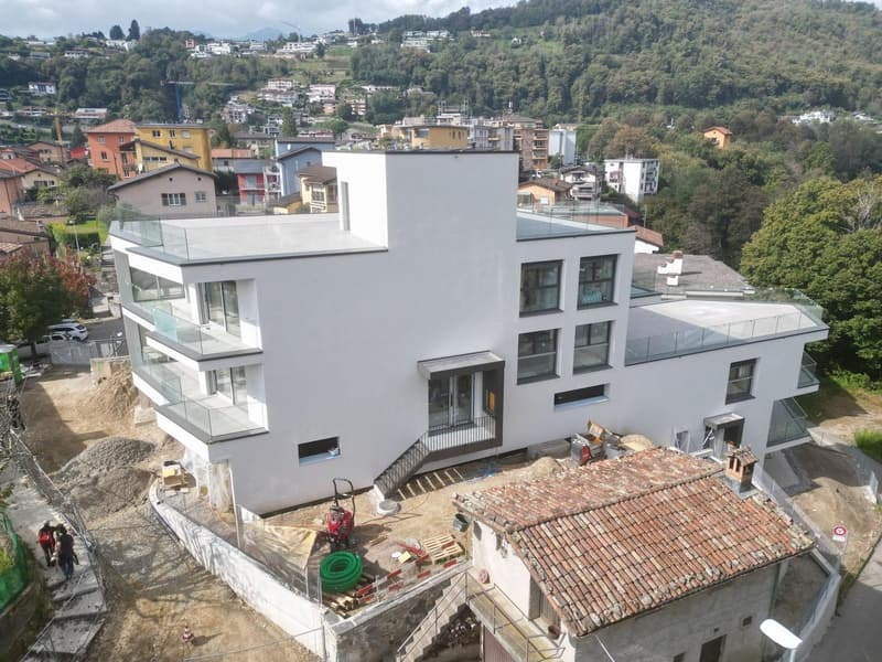 Modern house under construction, white exterior, glass balconies, terraced structure, machinery in yard