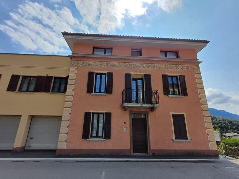 Three-story residential building with two garages, balcony, and windows with shutters.