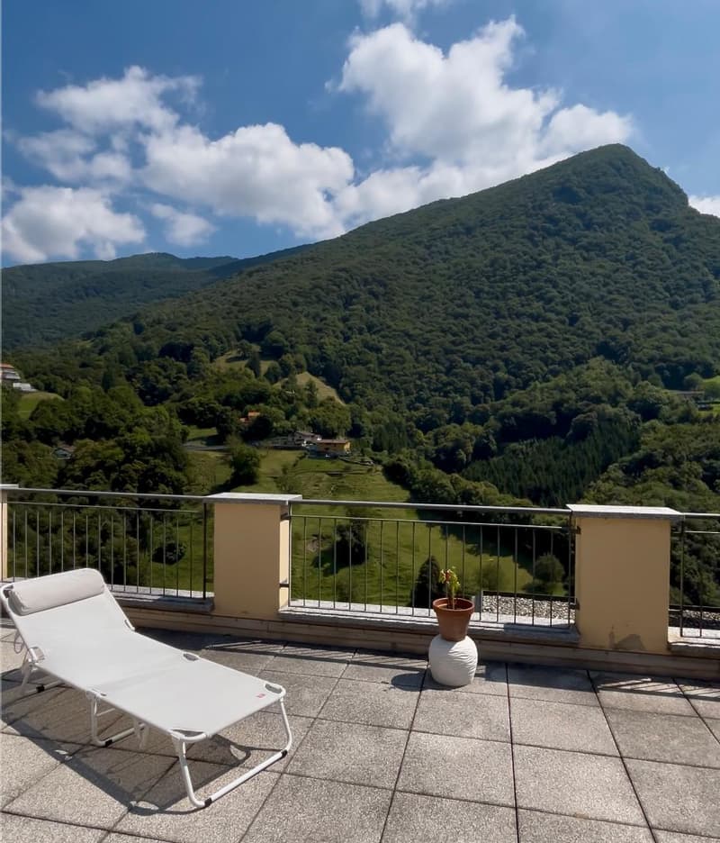 Terrace with lounge chair, tiled floor, metal railing, potted plant, distant mountain landscape with greenery and clouds.