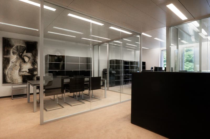 modern office space, large glass partitions, carpeted floor, long conference table, several chairs, large artwork on wall, shelves