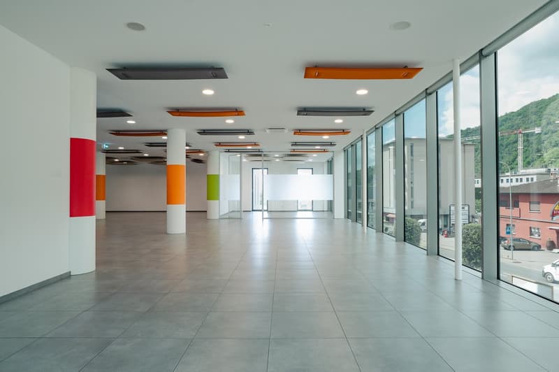Empty hallway with tiled floors, large glass windows, visible pillars with different colored stripes, street view outside