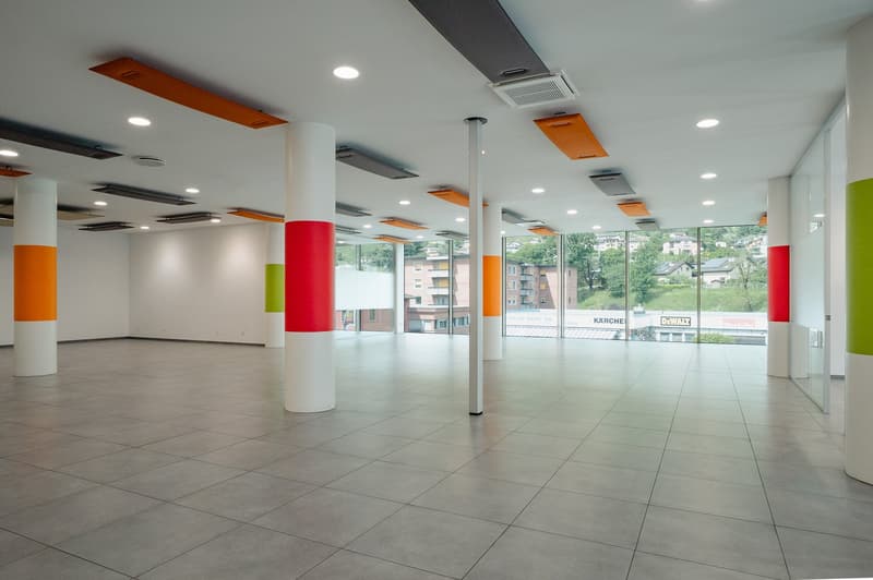 Large open space with white ceiling, colorful columns, gray tiles, large windows, glass doors