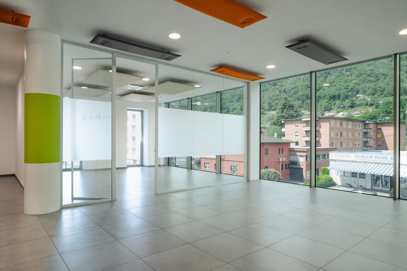 Open room with large glass walls, modern tile flooring, ceiling lamps, pillar in corner