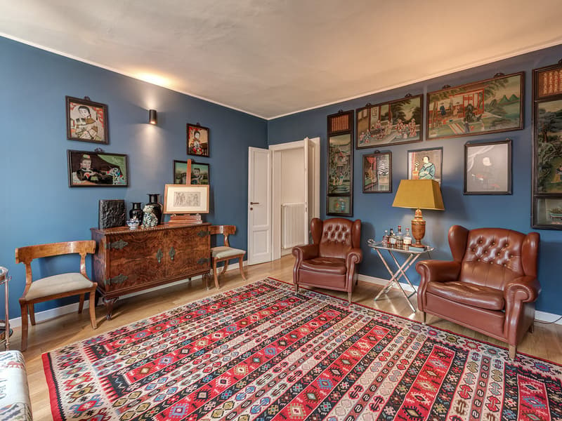 a cozy room with two leather armchairs, a wooden cabinet, a desk, and a large rug, decorated with framed artworks and a lamp