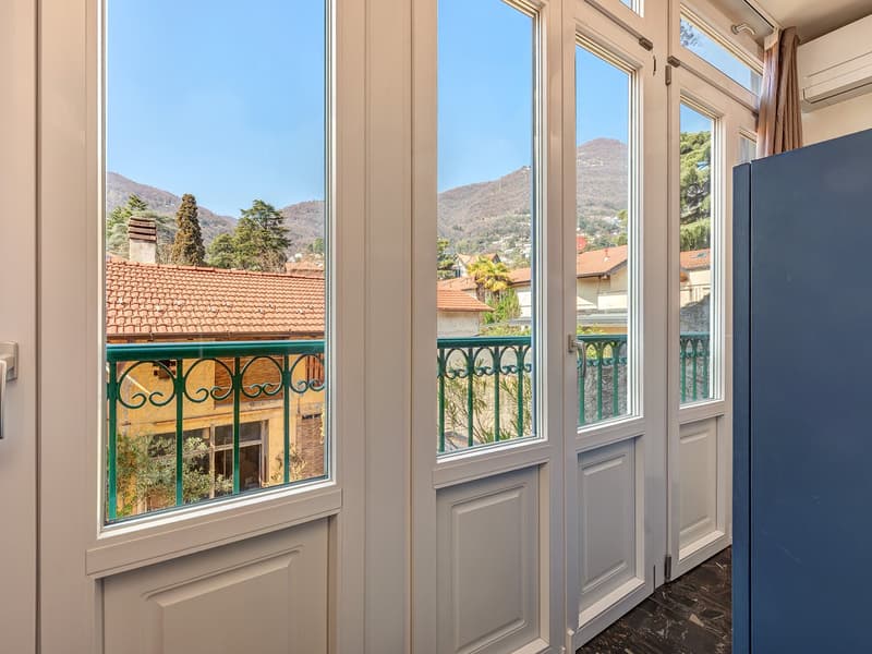 white interior, green railings on balcony, large windows, wooden floor, air conditioner