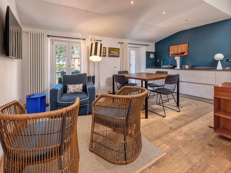 blue couch, wooden table, wooden chairs, television, kitchen with modern appliances