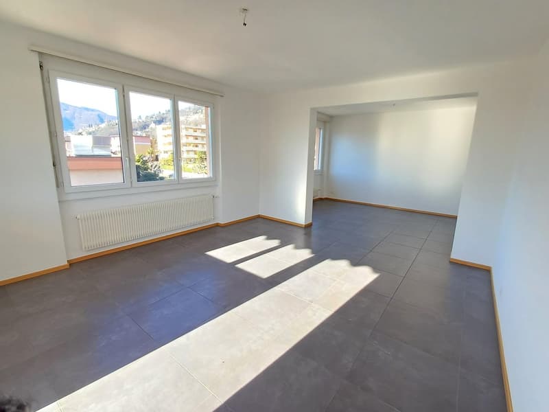 Empty room, grey tiled floor, white walls, large windows, radiator