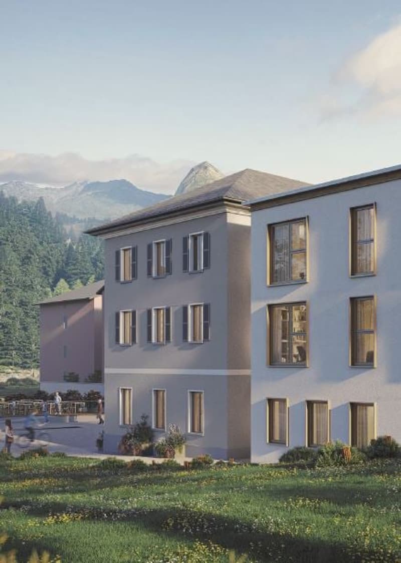 Modern apartment building with multiple windows, green lawn in front, mountains in the background.