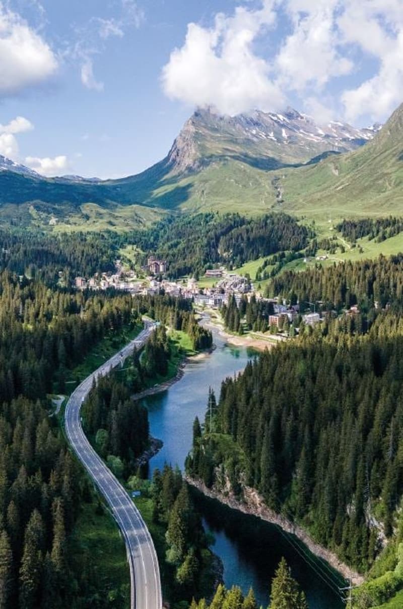 Panoramic aerial shot of scenic mountain valley with road, river, and village.