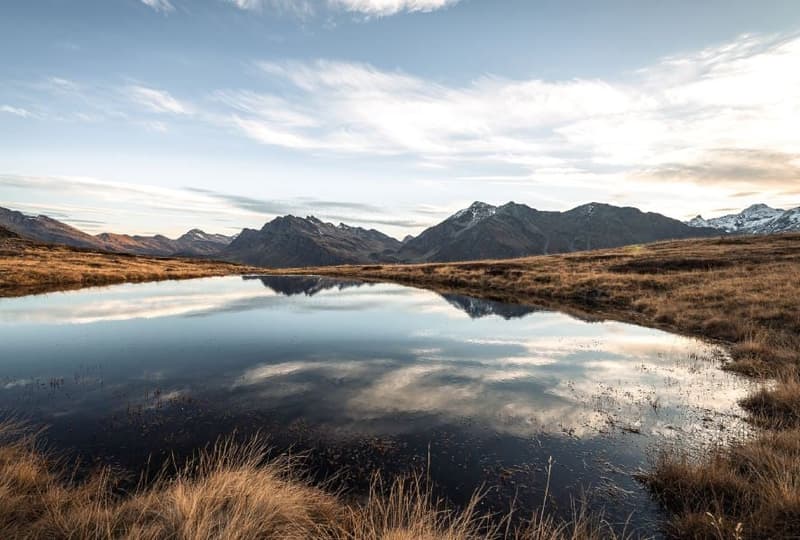 mountains in the background, water pond, dry grass, sky, clouds