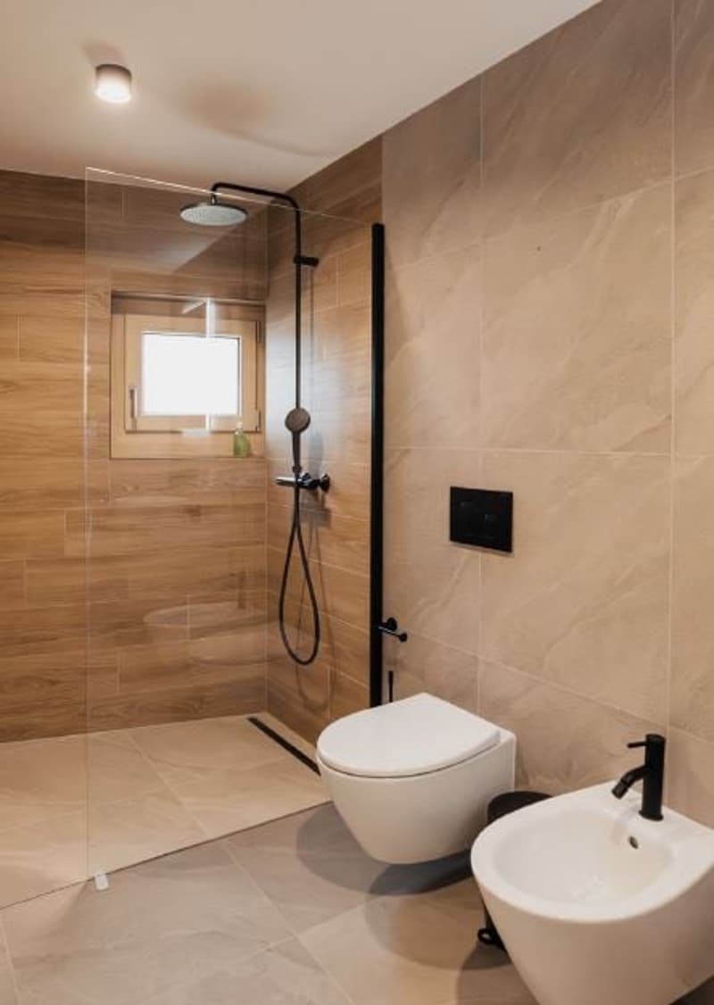 Modern bathroom with shower area, white toilet, sink, wooden tiles, glass door, small window