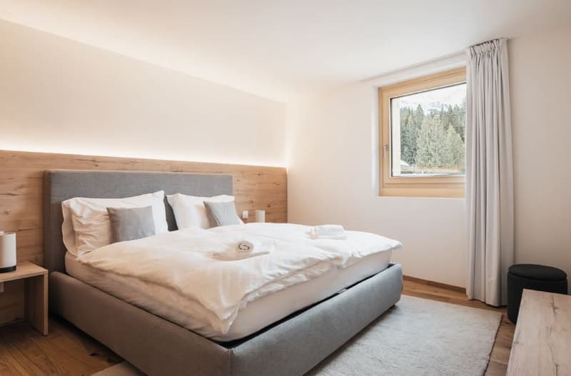 Spacious bedroom with a large bed, wooden accents, white linens, nightstand, window with a view of the mountains, rug