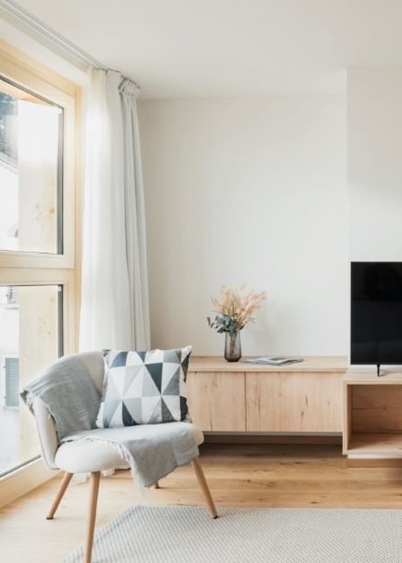 light-filled room, wooden chair, TV, wooden side table with flowers, light curtains, light wooden floor