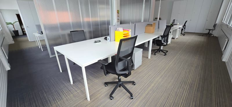 Empty office space with desks, chairs, and white partitions.