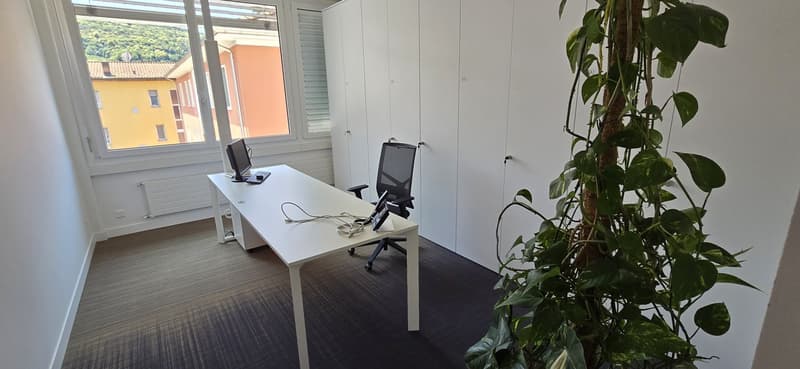 an empty office room with a desk, two office chairs, computer monitors, a cabinet, a window with view to a building