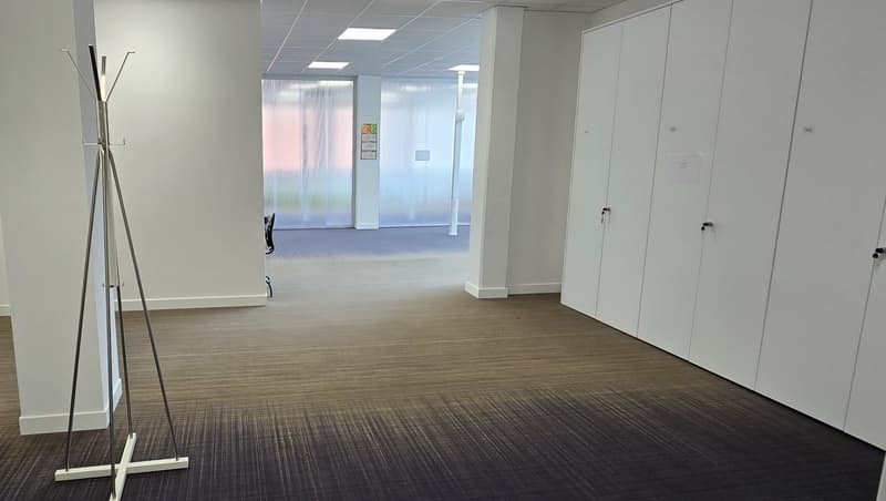 Empty office space with white walls, gray floor, glass door, white cabinets, coat rack