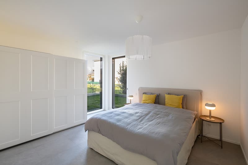 modern bedroom with white walls, gray bed, yellow pillows, white ceiling lamp, white nightstands, sliding glass doors, garden view