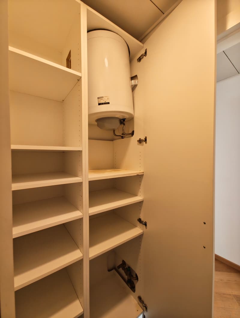 White shelves, white door, white pipework, water heater installed on ceiling, blank white wall