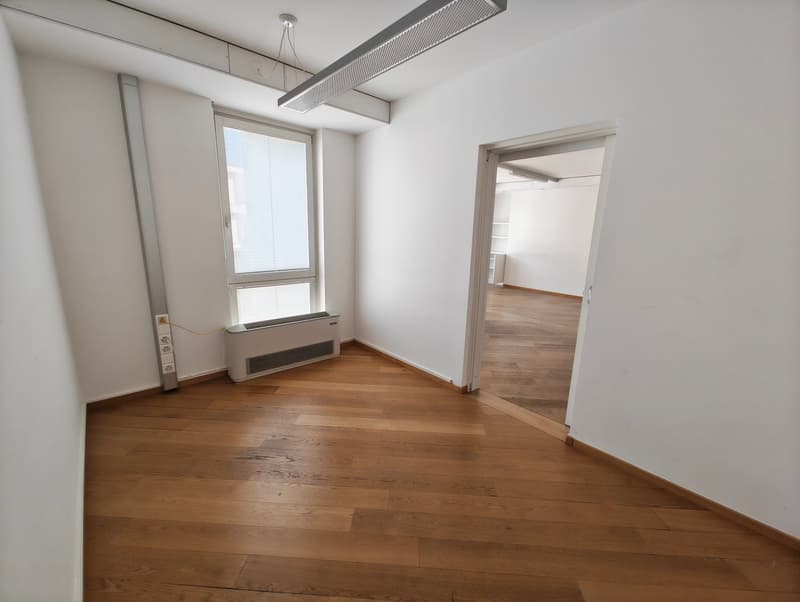 Empty room, wooden floors, white walls, large window, open door to another room, heater mounted on the wall